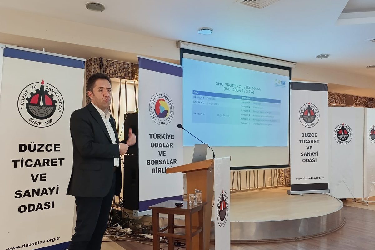 Ticaret ve sanayi odasında sera gazı sunumu; ekranda GHG Protokol ve ISO 14064 kapsam tablosu