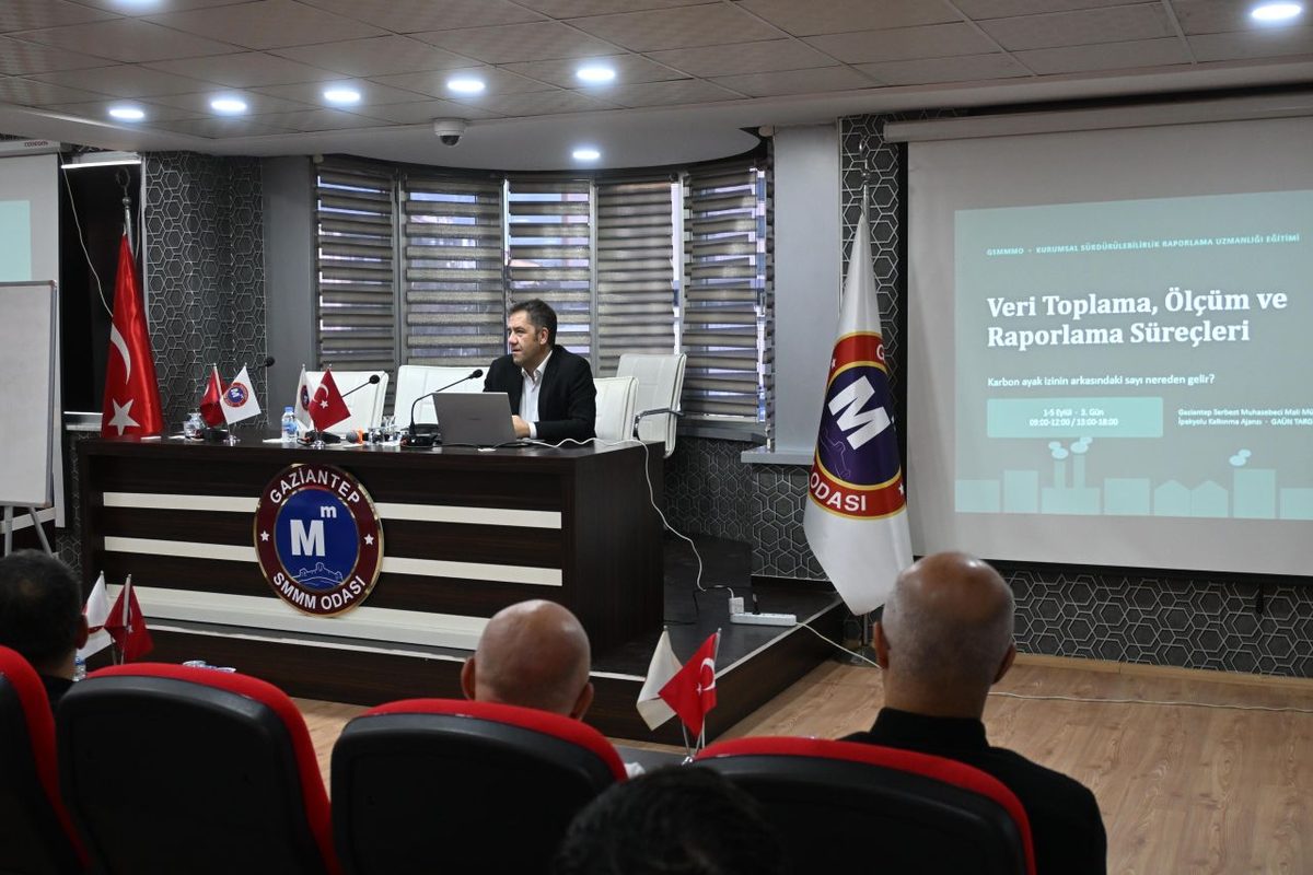 Meslek odası salonunda kurumsal sürdürülebilirlik raporlama eğitimi; ekranda veri toplama ve ölçüm süreçleri sunumu